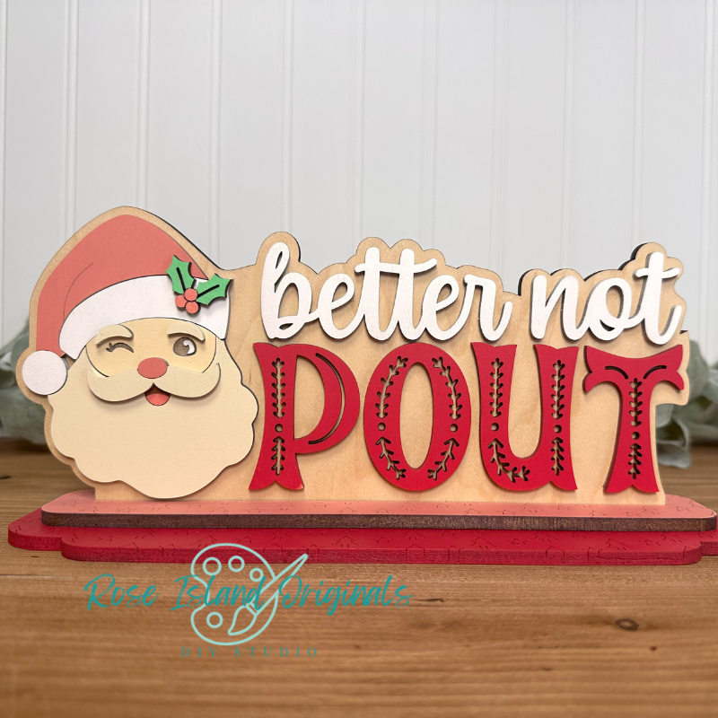 Wooden decorative sign with Santa face and 'better not pout' text on a wooden surface.