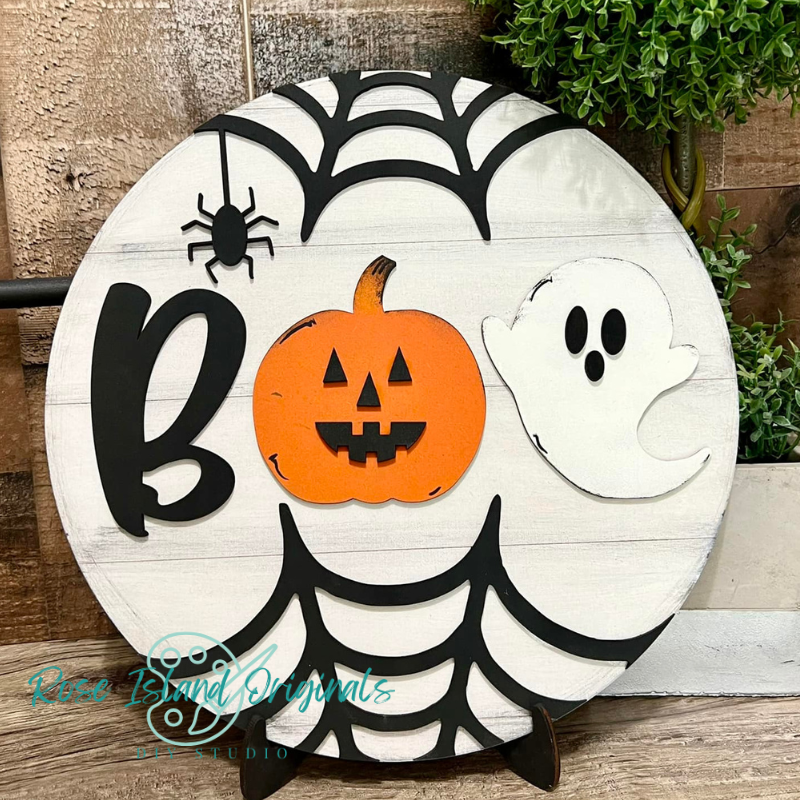 Halloween-themed decorative sign with a pumpkin, ghost, and spider on a wooden background.