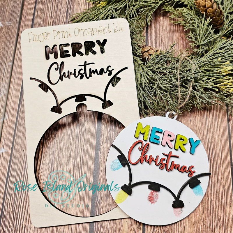 Finger print ornament kit with 'Merry Christmas' design on a wooden surface with greenery.
