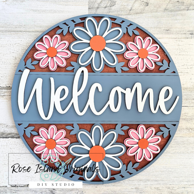 Decorative round sign with flowers and 'Welcome' text on a wooden background
