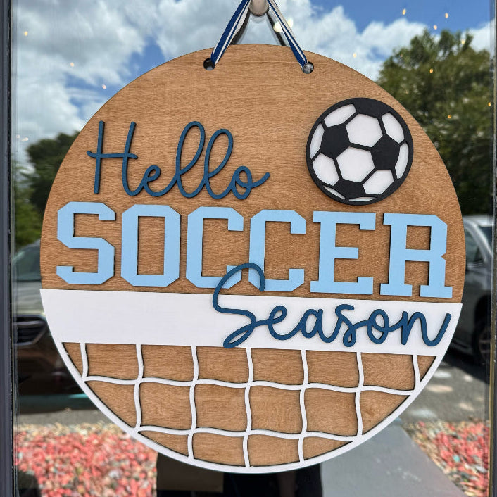 Decorative sign with 'Hello Soccer Season' text and a soccer ball graphic, hanging on a door.