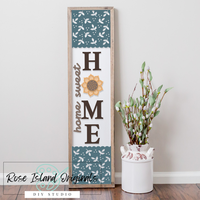 Decorative sign with 'Home Sweet Home' text and floral patterns next to a white vase with greenery on a wooden floor.
