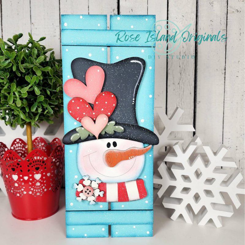 Decorative snowman box with heart designs on a wooden surface with a plant and snowflake decoration.