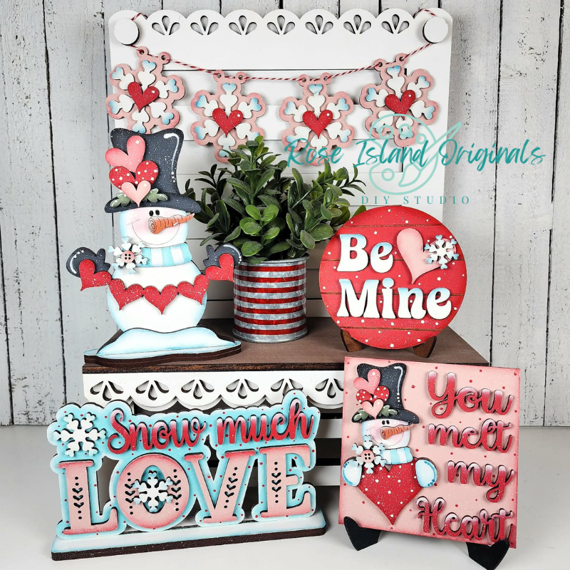 Decorative signs with snowmen and Valentine's Day phrases on a white surface.