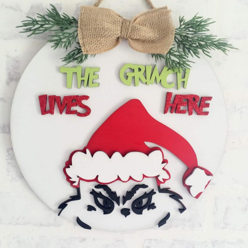 Decorative sign with Grinch face and text 'The Grinch Lives Here' on a white background.