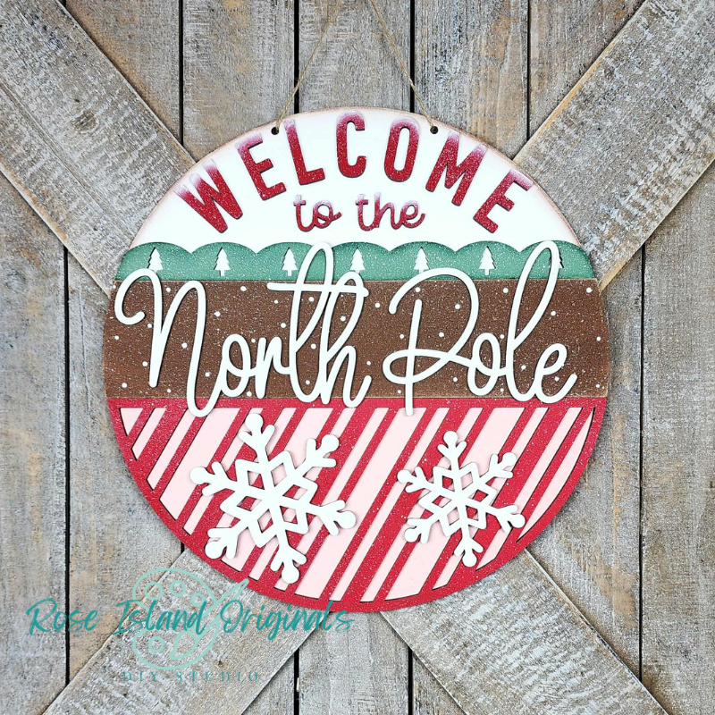 Round decorative sign with 'Welcome to the North Pole' text on a wooden background