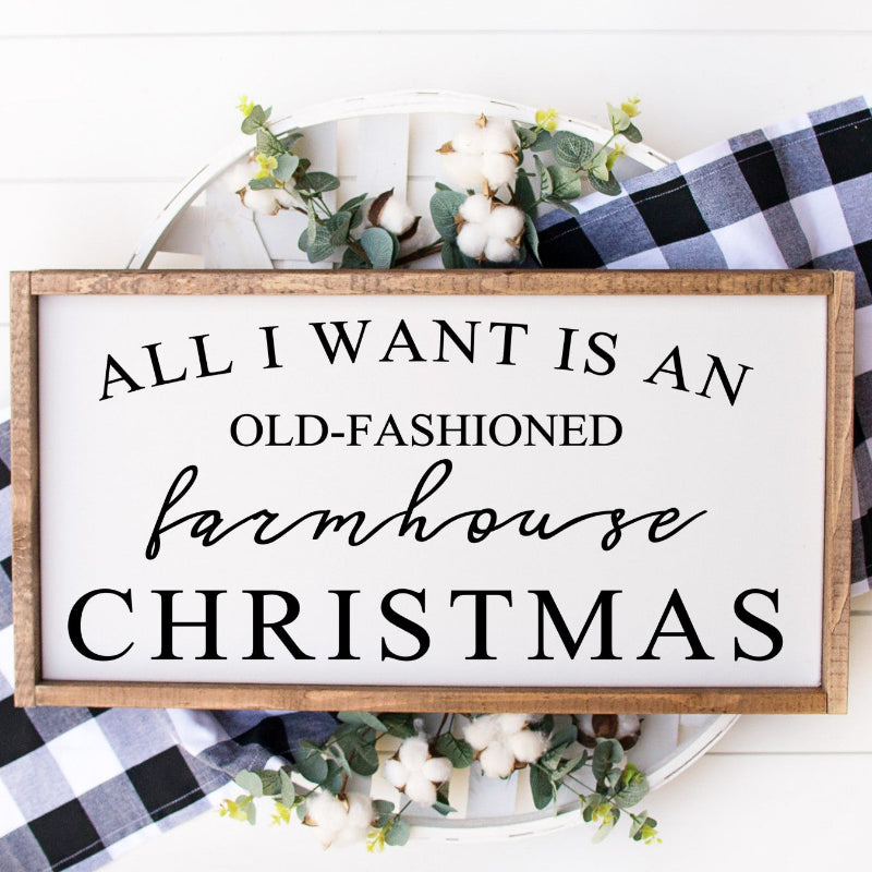 Decorative sign with text 'All I Want is an Old-Fashioned Farmhouse Christmas' on a white background with plaid fabric and greenery.