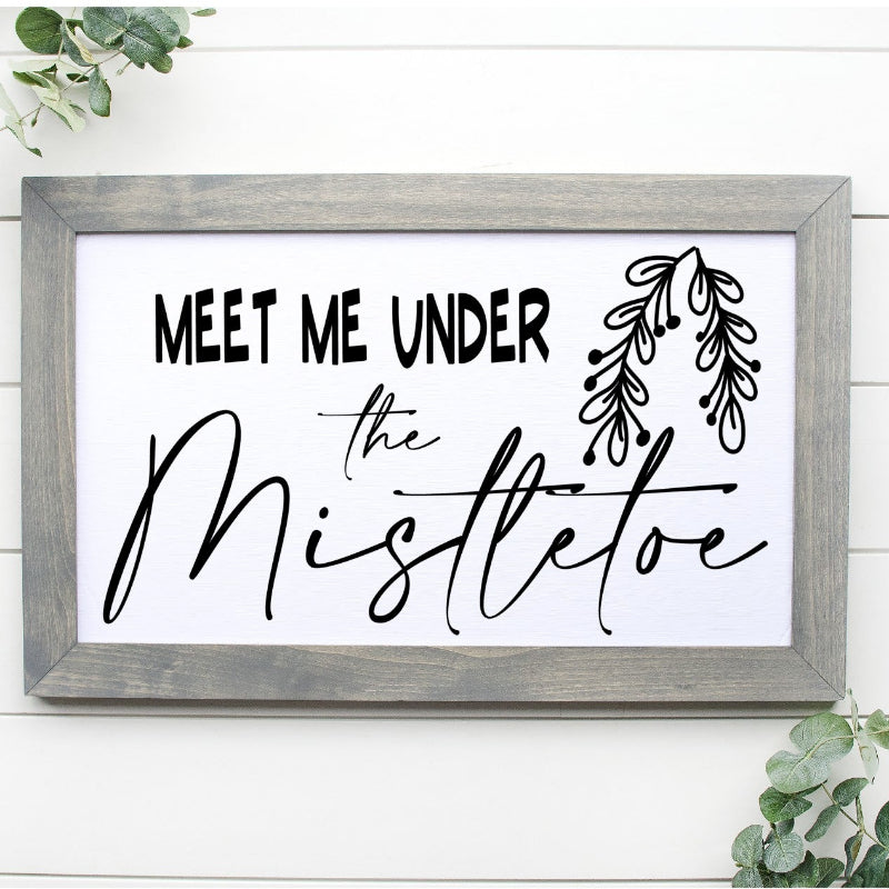 Framed sign with 'Meet Me Under the Mistletoe' text on a white background with greenery.