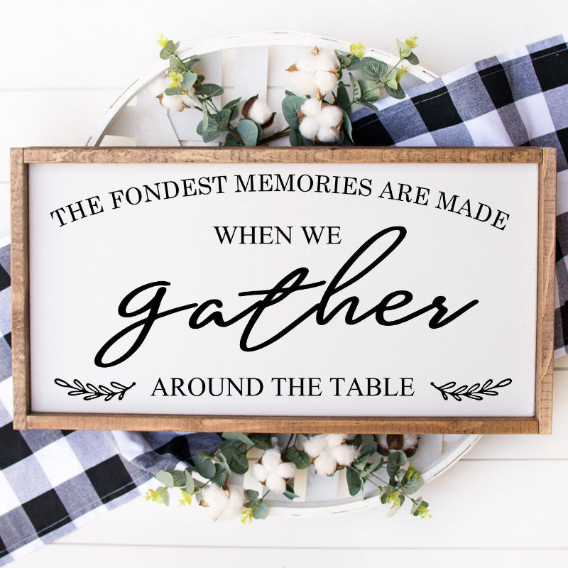 Decorative sign with text 'The fondest memories are made when we gather around the table' on a white background with checkered cloth.