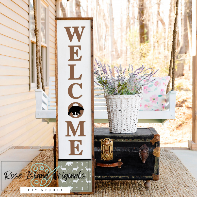 Wooden 'Welcome' sign with bear silhouette on a porch with a basket of flowers and chair.