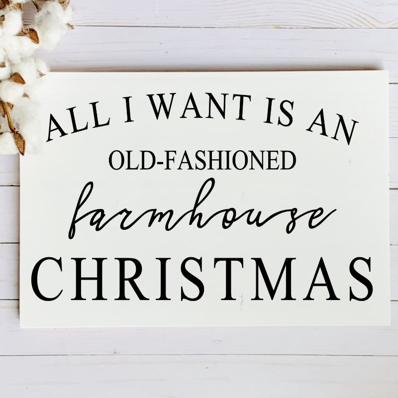 Sign with text 'All I want is an old-fashioned farmhouse Christmas' on a white wooden background.