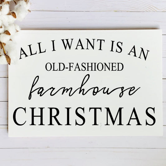 Sign with text 'All I want is an old-fashioned farmhouse Christmas' on a white wooden background.