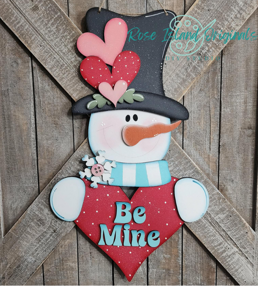 Wooden snowman decoration with heart and 'Be Mine' text on a wooden background