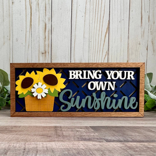Decorative sign with sunflowers and text 'Bring Your Own Sunshine' on a wooden background.