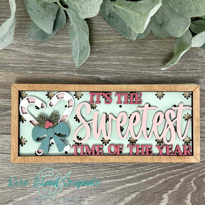 Decorative sign with 'It's the Sweetest Time of the Year' text on a wooden surface with greenery.