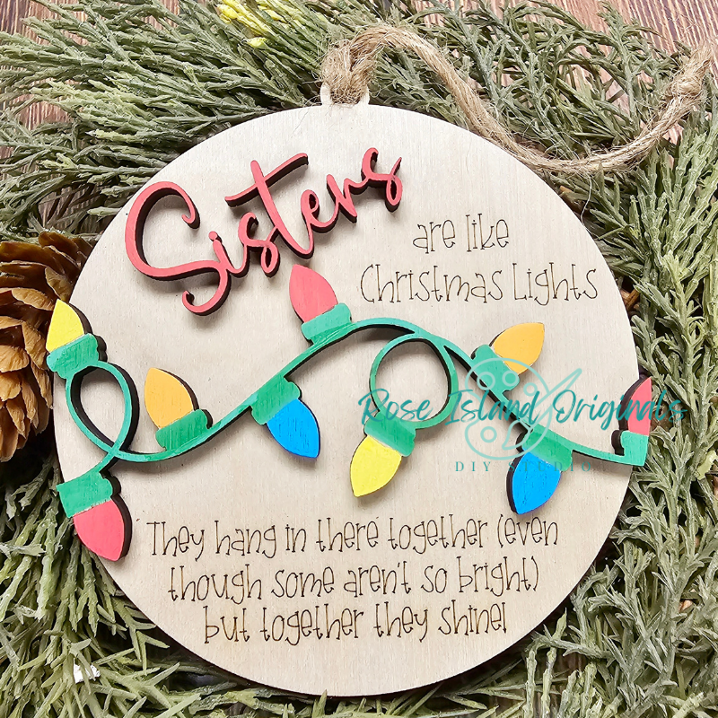 Decorative Christmas ornament with 'Sisters are like Christmas Lights' text on a wooden background.