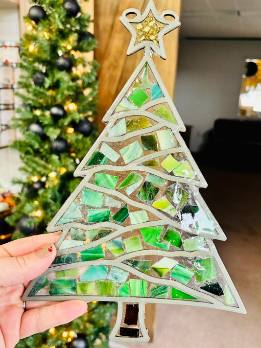 Mosaic Christmas tree decoration held in front of a decorated Christmas tree.