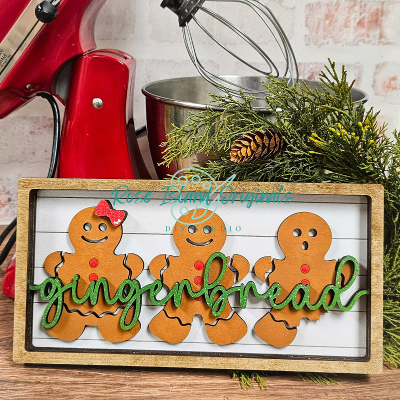 Decorative sign with gingerbread men and 'gingerbread' text in front of a red mixer and greenery.