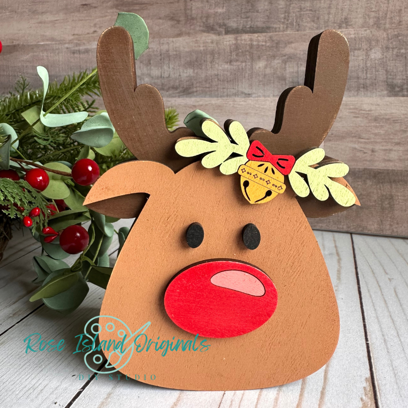 Wood reindeer decoration with green leaves and red berries on a wooden surface.