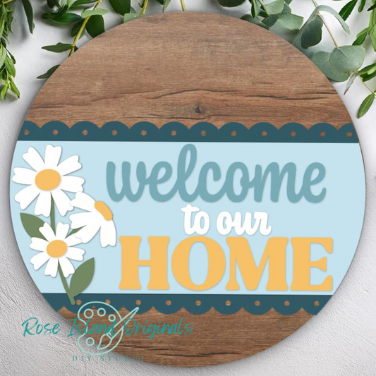 Round wooden sign with 'welcome to our home' text and daisy flowers on a light blue background.