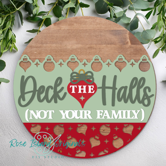 Round wooden sign with Christmas design and text 'Deck the Halls (Not Your Family)' on a white background with greenery.