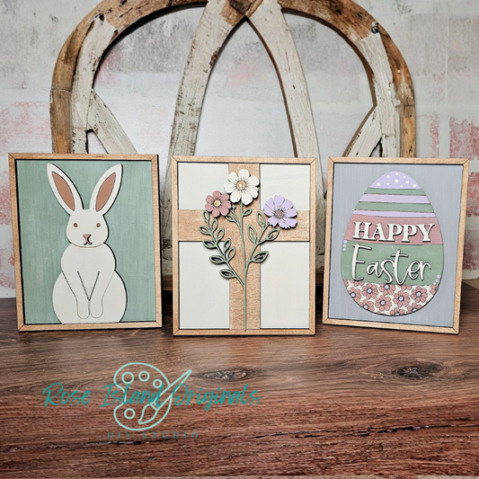 Three framed Easter-themed artworks on a wooden surface with a rustic background.