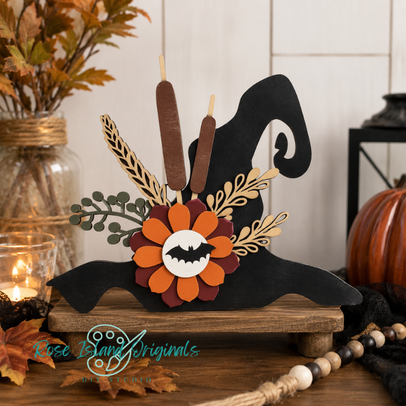 A decorative Halloween-themed wooden cutout shaped like a witch hat, displayed on a small wooden stand. The design includes layered orange and burgundy flower petals with a white center, gold leafy accents, two brown candlesticks, and a black witch hat silhouette.