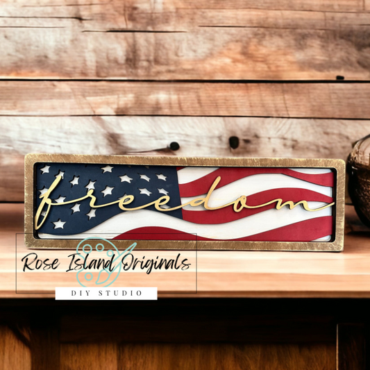 Wooden sign with American flag design and 'freedom' text on a wooden surface, featuring Rose Island Originals branding.