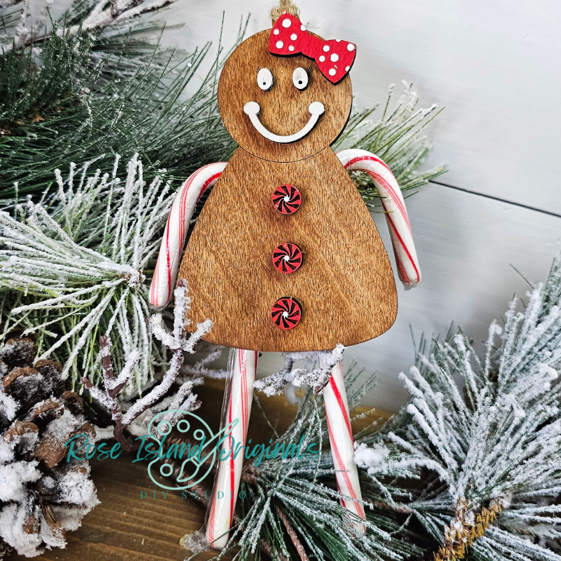 Wooden gingerbread man ornament with candy canes and a red bow on a Christmas tree background.