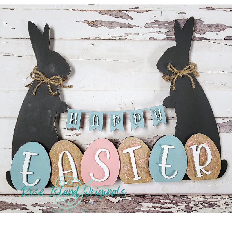 Decorative sign with black bunny shapes and colorful 'Happy Easter' eggs on a wooden background.