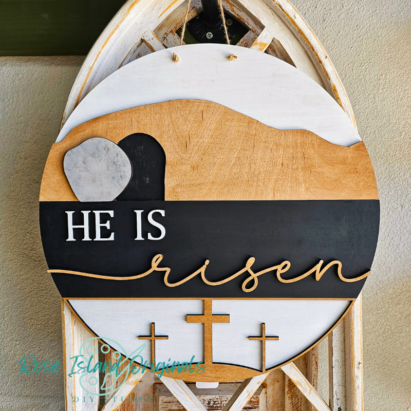 Decorative sign with 'He is risen' text and cross designs on a wooden background.