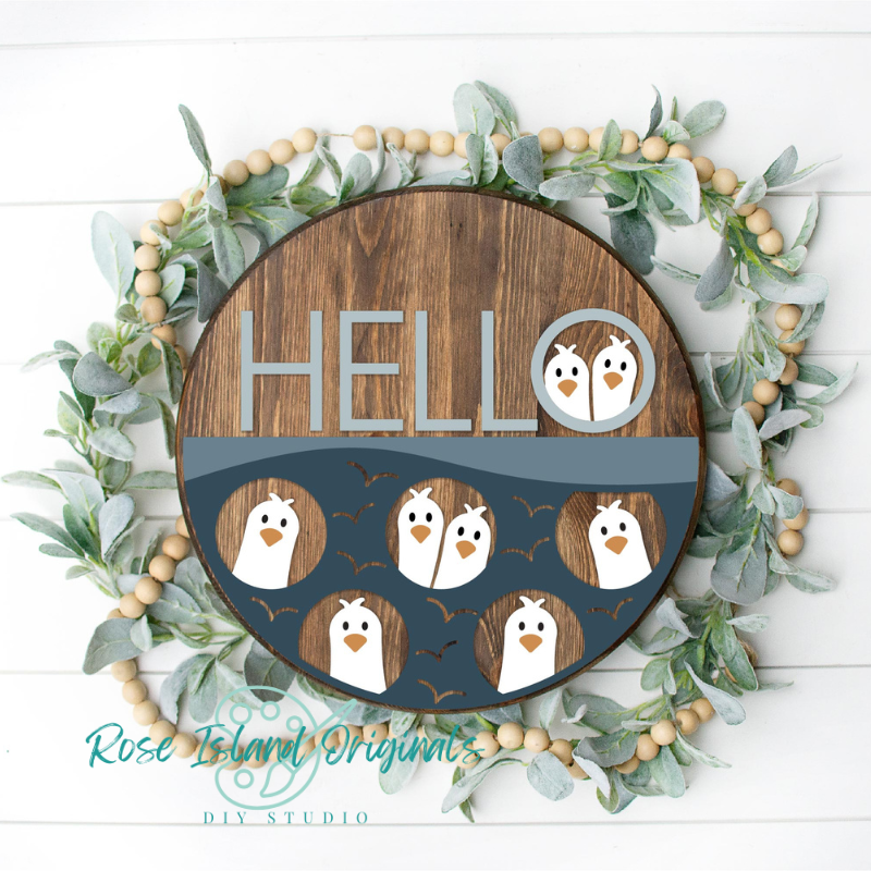 Decorative sign with penguin design and 'HELLO' text, surrounded by greenery and wooden beads.