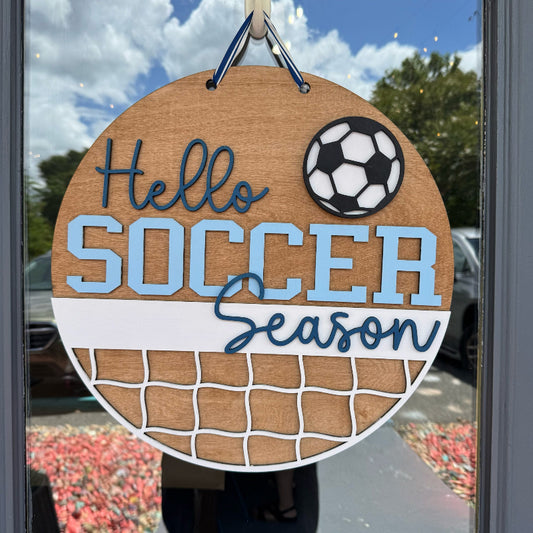 Decorative sign with 'Hello Soccer Season' text and a soccer ball graphic, hanging on a door.