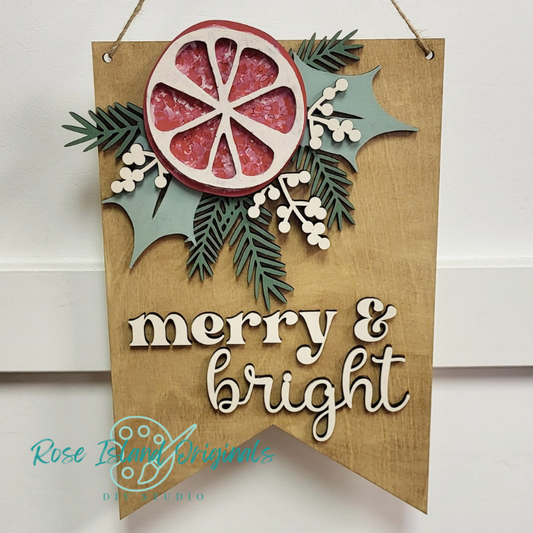 Decorative sign with a orange slice, leaves, and the text 'merry & bright' on a wooden background.