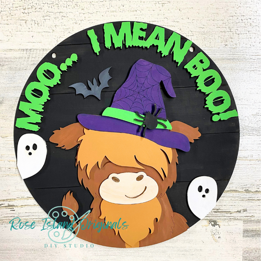 Halloween-themed decoration with a highland cow wearing a witch hat and text 'I MEAN BOO!' on a black background.