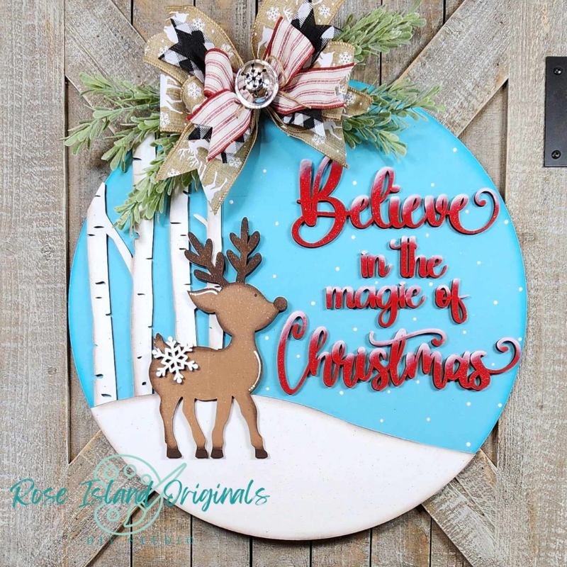 Decorative Christmas sign with reindeer, bow, and text 'Believe in the magic of Christmas' on a wooden background.