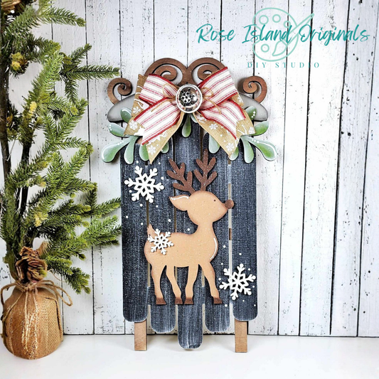 Decorative wooden panel with reindeer and bow design on a white wooden background