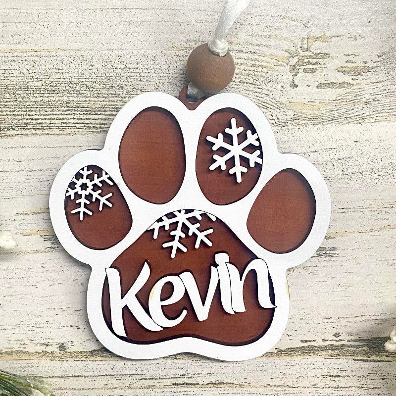 Paw-shaped ornament with your pet's name and snowflake designs on a wooden surface.