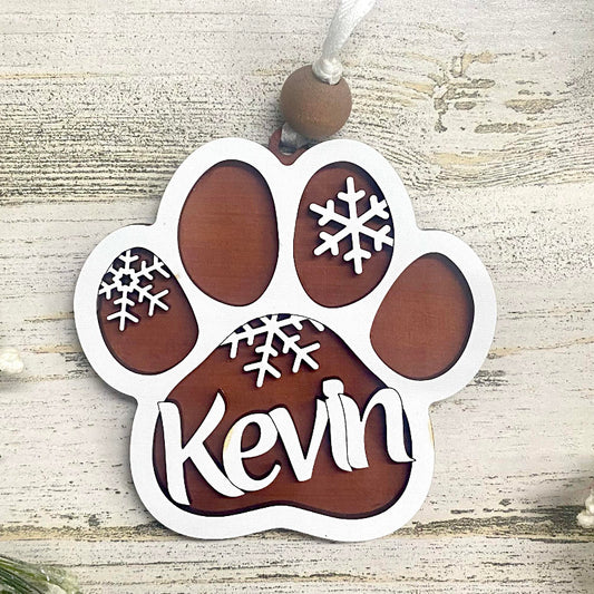 Paw-shaped ornament with your pet's name and snowflake designs on a wooden surface.