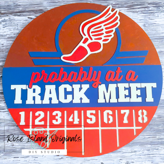 Circular sign with track and field design and text 'Probably at a Track Meet' on a wooden background.