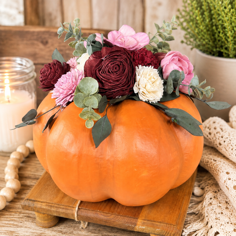 Pumpkin with colored flowers and greenery displayed on a table top. 