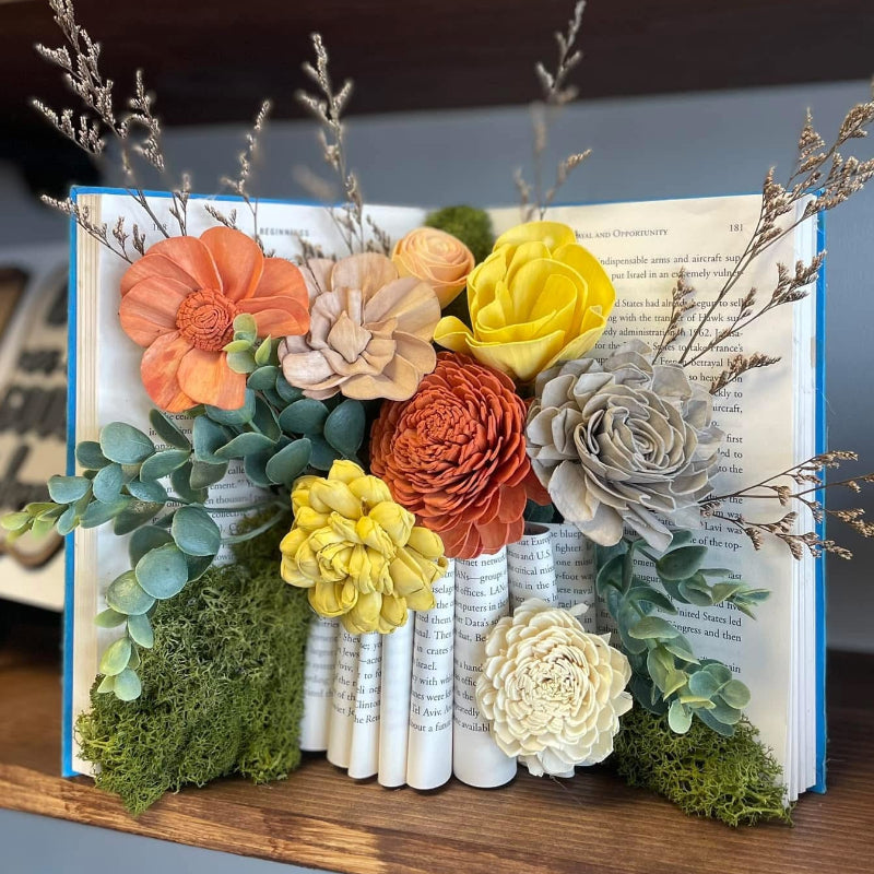 Dyed wood flowers arranged in a book displayed on a shelf.