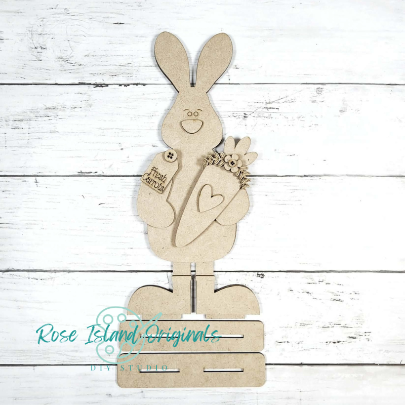 Wooden bunny decoration with a heart and flowers on a white wooden background, branded 'Rose Island Originals'.