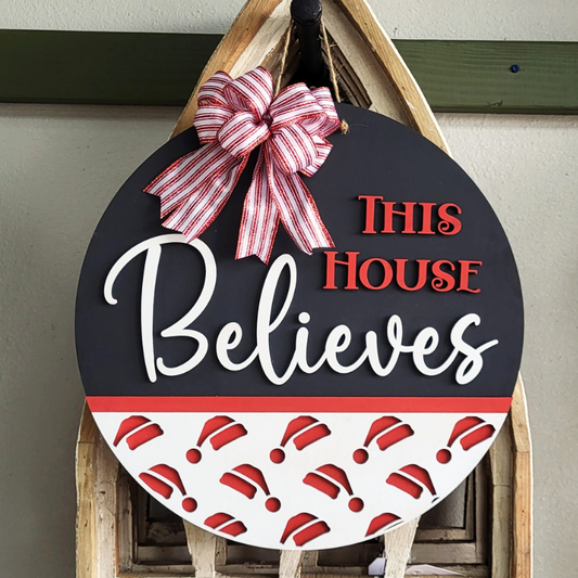 Decorative sign with 'This House Believes' text and a red bow on a wooden stand.