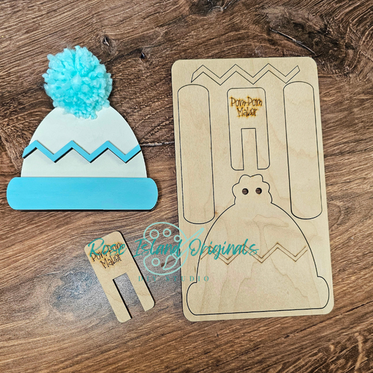Wooden craft item shaped like a beanie with a pom-pom, a wooden template, and a small wooden tool on a wooden surface.