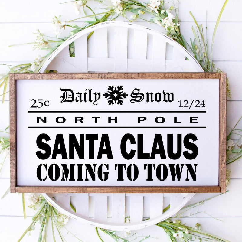 Decorative sign with text 'Daily Snow, North Pole, Santa Claus Coming to Town' on a white background with greenery.