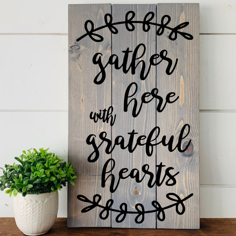 Wooden sign with 'gather here with grateful hearts' text on a white wall background