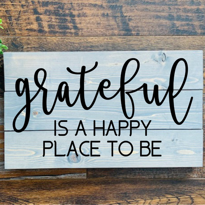 Wooden sign with 'grateful is a happy place to be' text on a wooden background