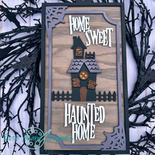 Decorative sign with 'Home Sweet Haunted Home' text and haunted house design on a wooden background.