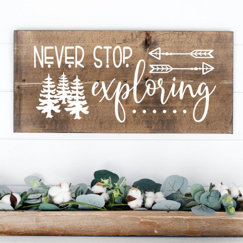 Wooden sign with 'Never stop exploring' text on a white surface with decorative elements.